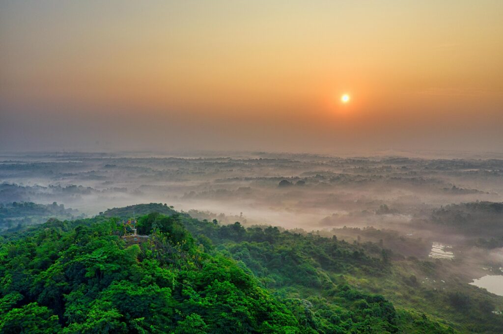 Stunning aerial view of a sunrise over a lush green landscape with mist creating a serene atmosphere.