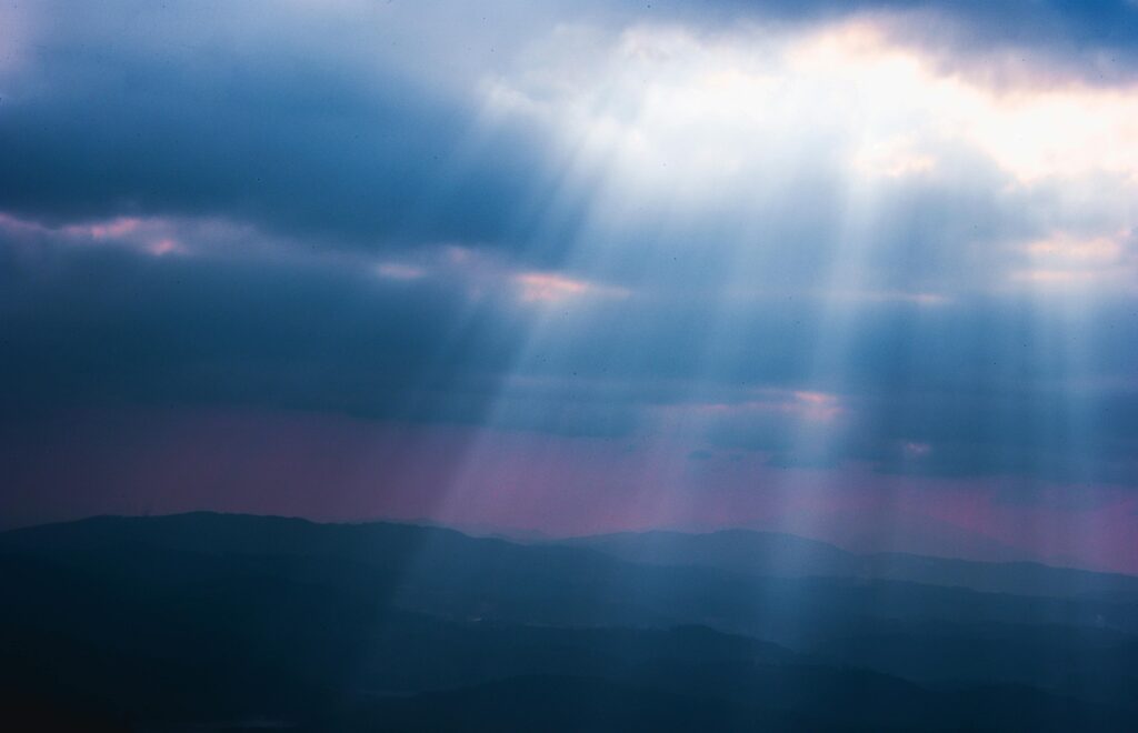 Sunrays piercing through clouds over a scenic landscape during twilight, showcasing nature's beauty.